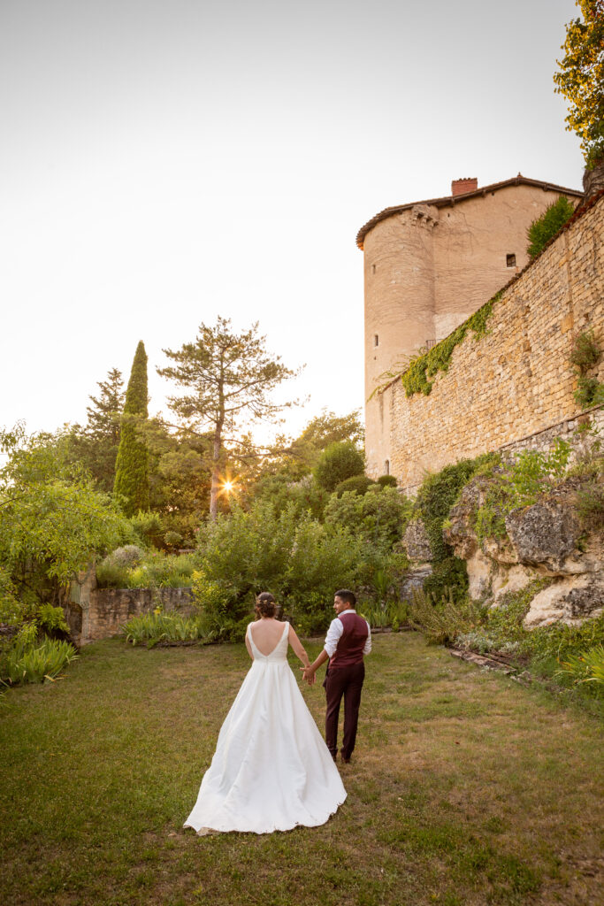 deux jeunes mariés dans le parc d'un château, qui se tiennent par la main devant le coucher du soleil