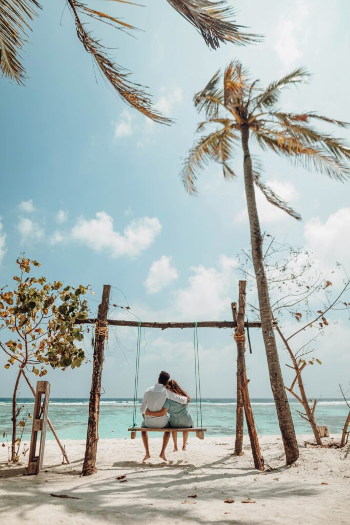 un homme et une femme qui se font un câlin sur une balançoire sur une plage de sable blanc face à l'océan