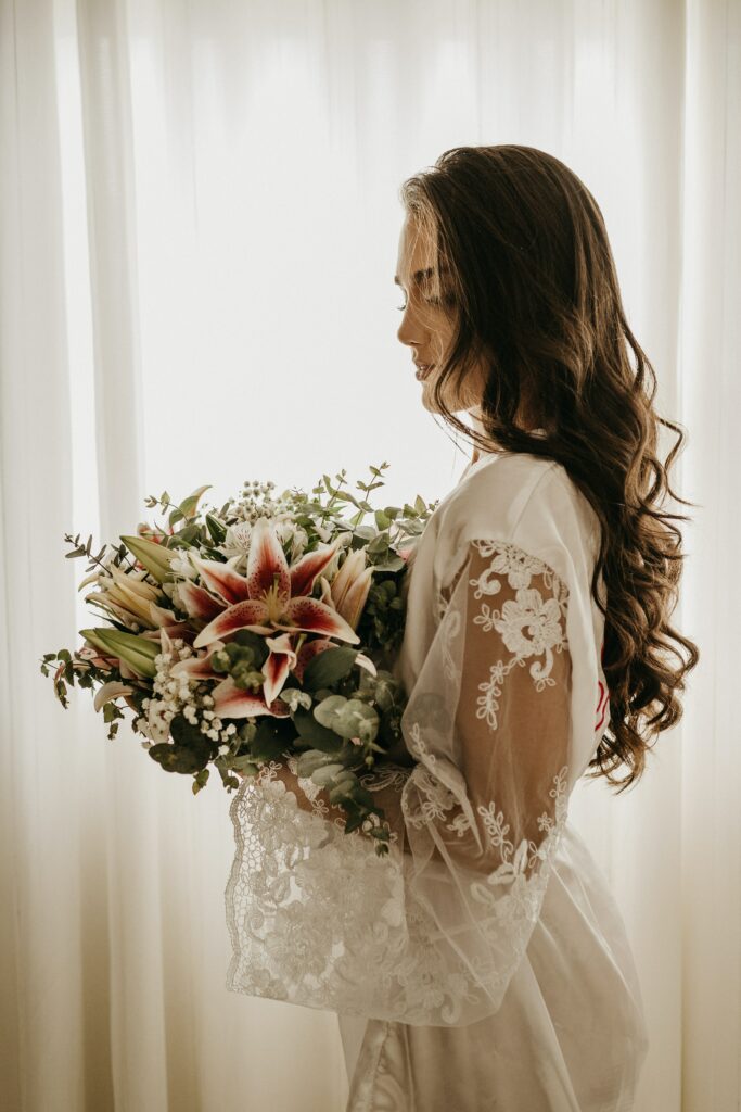 Femme habillée avant son mariage et qui tient un bouquet de fleurs fraiches